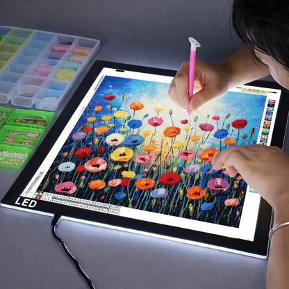 Person using a pink pen to color a floral design on an LED art board.