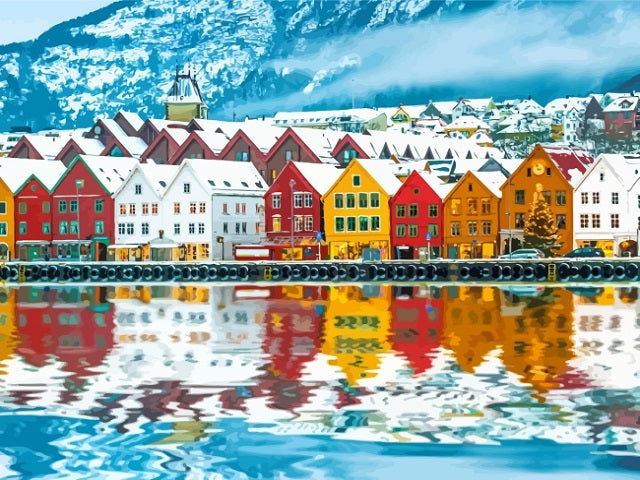 A scenic view of colorful houses with snow-covered roofs along a waterfront, with mountains in the background and the buildings reflected in the water. Norway Town - Diamond Painting
