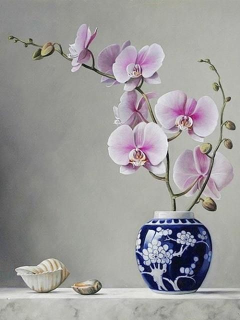 A still-life style painting of pink orchid flowers arranged in a blue-and-white ceramic vase on a light stone surface, with two seashells beside it against a soft gray background. Pink Orchid - Diamond Painting