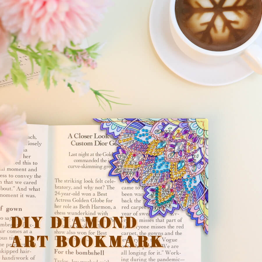 An open book with a colorful, ornate diamond art bookmark displayed on the right page. The bookmark features intricate mandala-style patterns in purple, gold, blue, and pink.